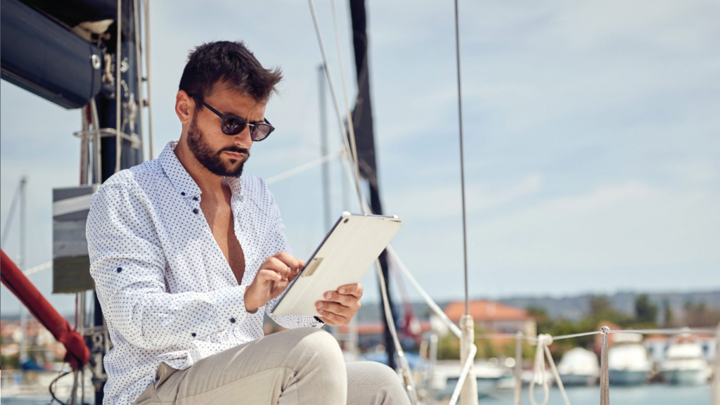 A man wearing sunglasses and a white patterned shirt is sitting on a boat.